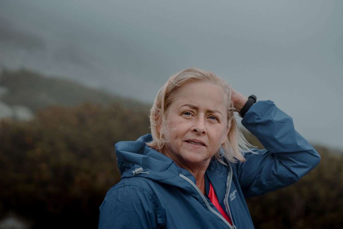 A senior woman outdoors wearing a blue jacket, looking contemplative under a cloudy sky