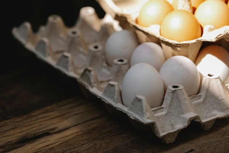 From above of fresh chicken eggs in carton container placed on wooden table in kitchen