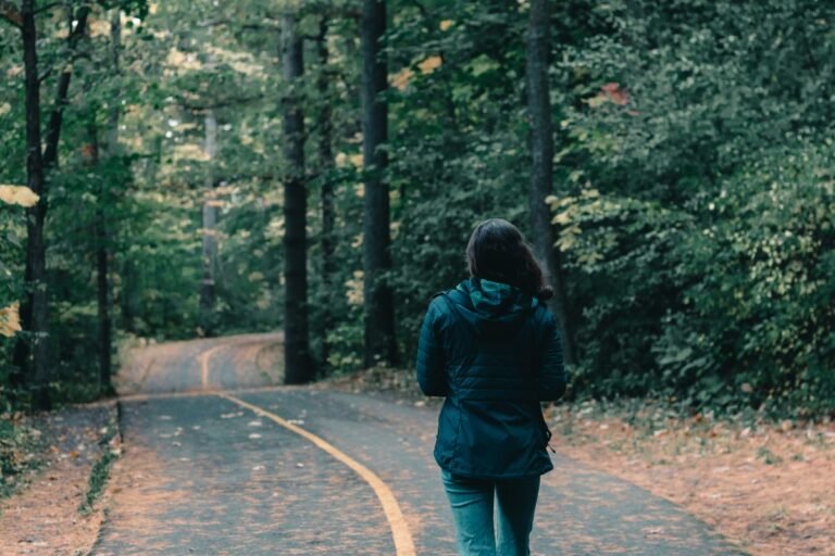 Rear view of a woman walking through a lush forest path during fall